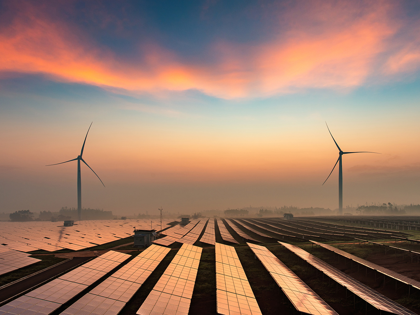 Solar panels in front of a windfarm at sunset