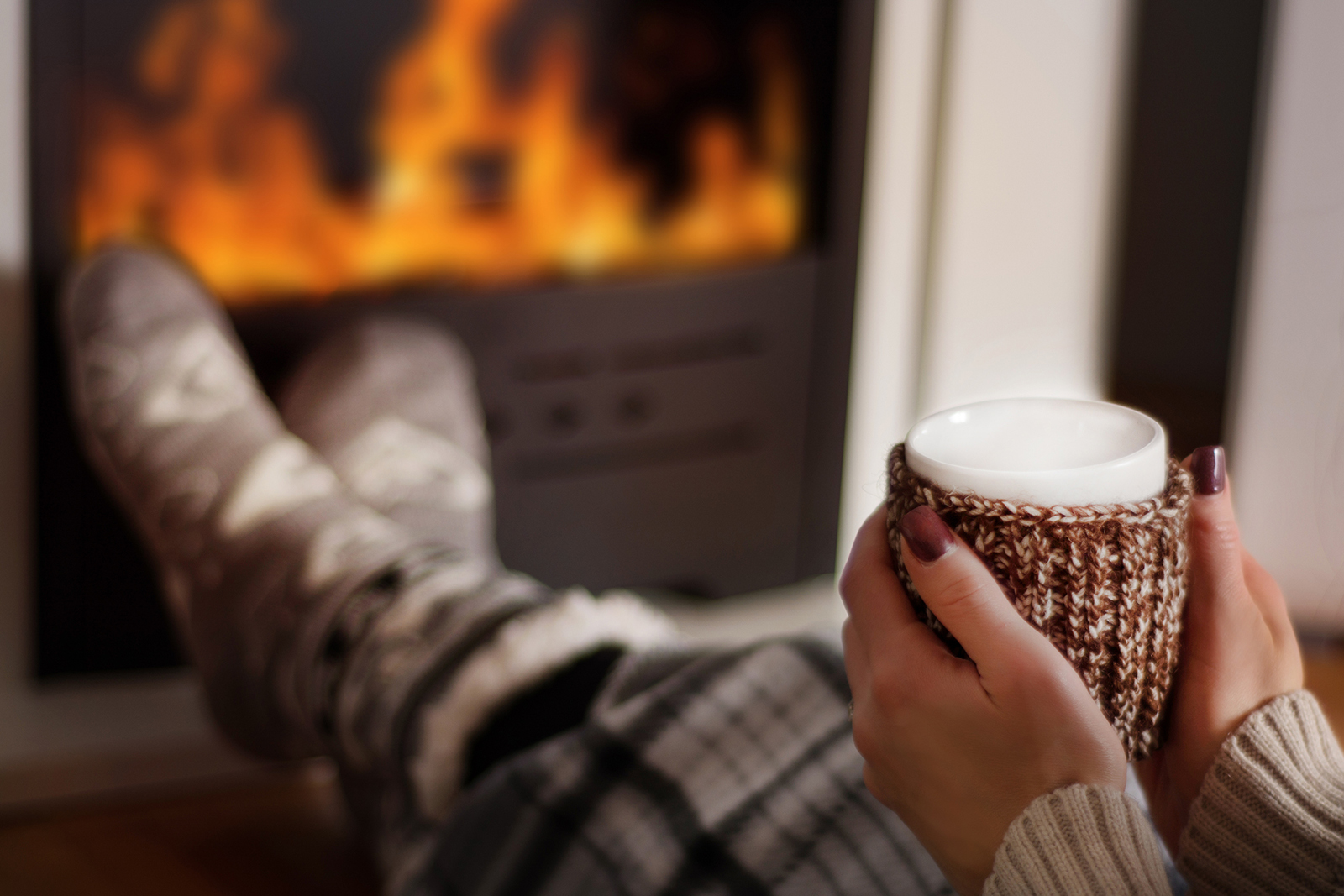 Young woman drinking hot tea in front of the gas fireplace